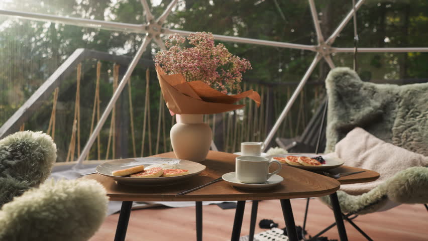 Breakfast on glamping cottage glass terrace. Low table paired with fluffy armchairs creates calm atmosphere to rest with stunning views. Perfect morning Royalty-Free Stock Footage #3399591753