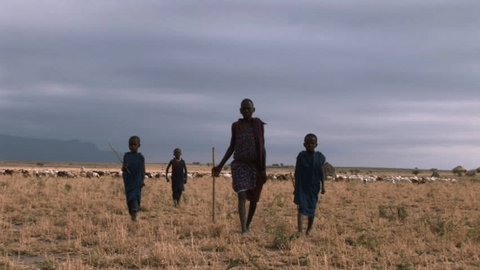 African brother and sister deprived children in a village walk towards camera. Storm sky.
