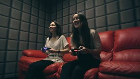 Two young girls playing video games with game controller on red sofa