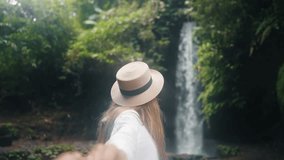 Follow me woman near tropical waterfall. Blonde smiling female tourist in straw hat holding man's hand following him to waterfall. Travel tourism vacation, summer holidays concept. Travelling couple. - Powered by Shutterstock - Get 15% off with code: PIKWIZARD15