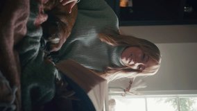 Vertical video close up of woman at home in winter jumper stroking pet French Bulldog and reading book - shot in slow motion