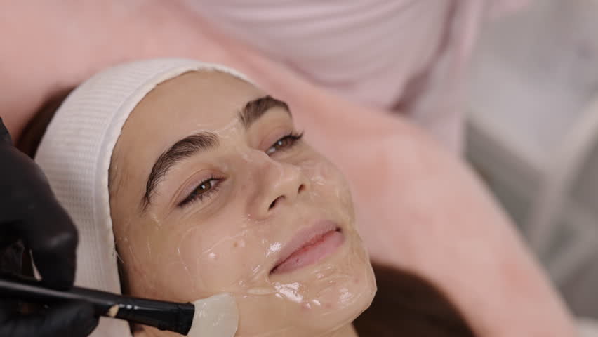 Treatment preparation, Wrinkle reduction, Beauty treatments. Cosmetologist carefully applies conductive gel to patient's skin with knuckle as prelude to RF lifting procedure. Royalty-Free Stock Footage #3399728435