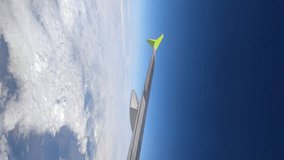 View through passenger airplane window of flying in the sky aircraft's wing in a sunny day. Clear blue sky with white clouds. Real time vertical video. Air travel and transportation theme.
