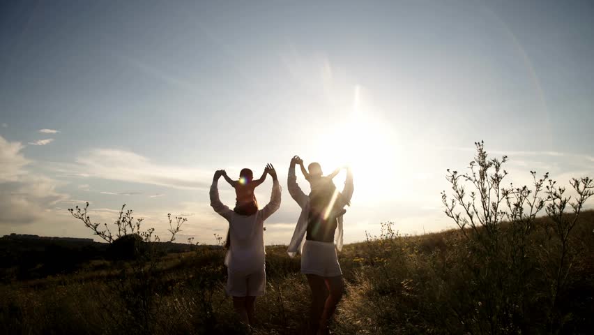 Happy family at sunset in a field. Silhouette of a group of people walking across a field. Happy child with parents holding hands. Concept of happy family, clothing advertising and family vacation