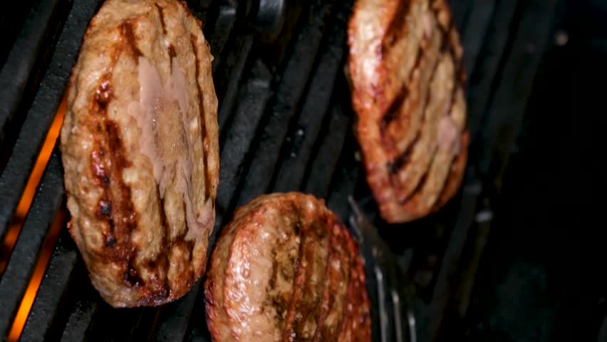vertical video Cooking burgers on a hot grill with a flame Beef cutlets cooked on a barbecue grill.Cooking beef and pork patty for party.