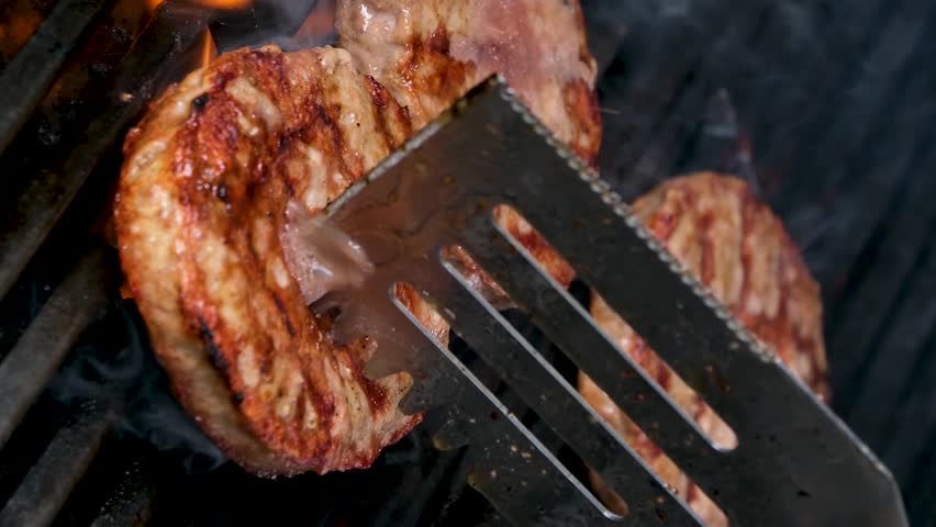 vertical video Cooking burgers on a hot grill with a flame Beef cutlets cooked on a barbecue grill.Cooking beef and pork patty for party.