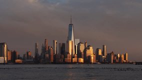 New York City skyline at sunset with passing clouds and World Trade Center skyscrapers from the Hudson River. Financial District of Lower Manhattan timelapse