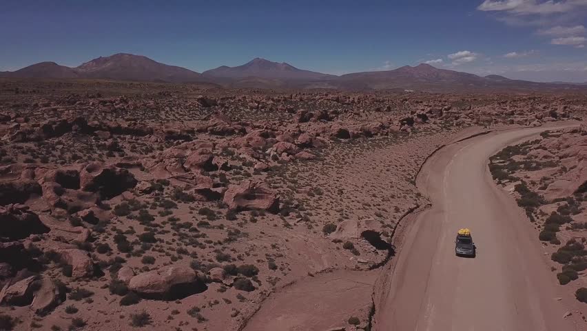 Aerial view of a 4x4 (4WD) on a dusty red road at the Eduardo Avaroa National Andean Wildlife Reserve, slowly lifting the view to open up to the valley of rocks, "Valle de Rocas" in Uyuni, Bolivia.
