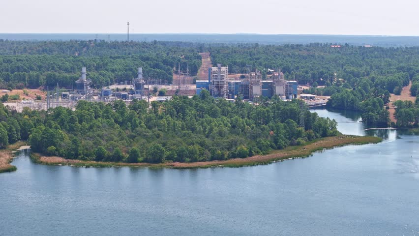 Moving quickly to the right above a lake that has a power plant behind it. Moving closer to the power plant and showing a portion of a lake inlet that goes all the way to the power plant footprint.