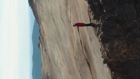 Man Stands on Mountain in Hverir Area Looking on Icelandic Landscape. Iceland. Aerial View. Drone is Orbiting. Vertical Video