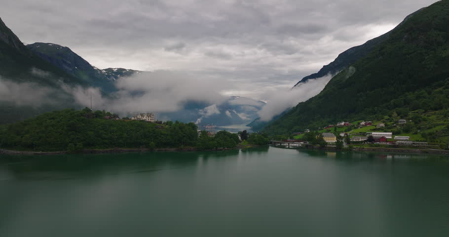 Drone parallax around Sandvatnet Lake with Odda and low clouds along alpine mountain of fjord