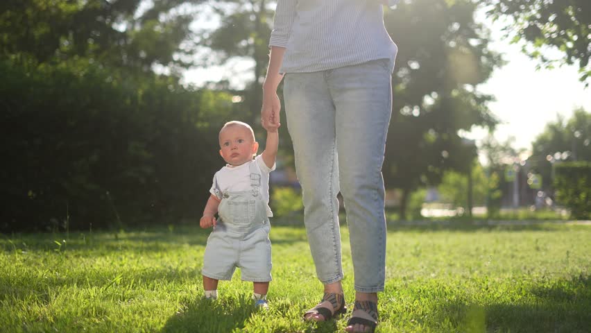 baby first steps. happy family kid dream concept. mom holding her son hand to learn to walk the first steps in park. baby first steps in nature. mom lifestyle teaches son to walk