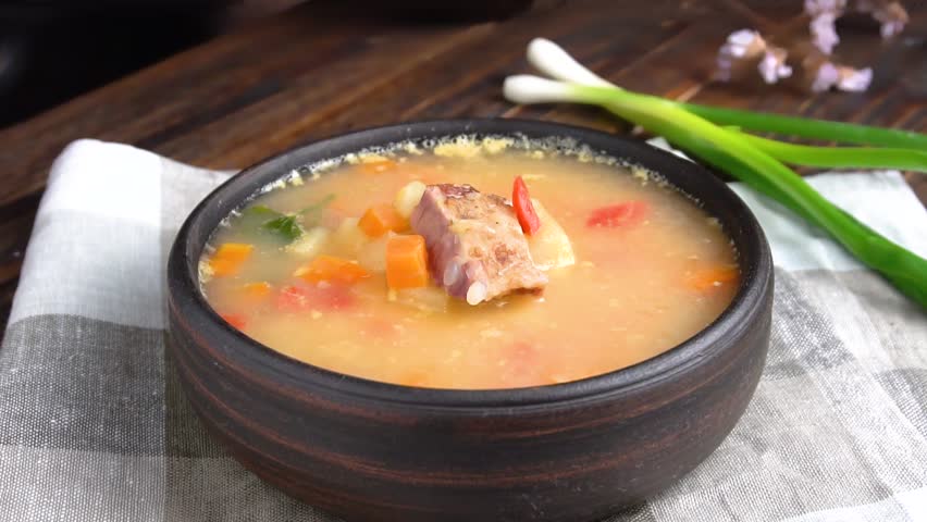 Adding chopped green onions to flavorful pea soup with smoked ribs. Slow motion. Close-up.