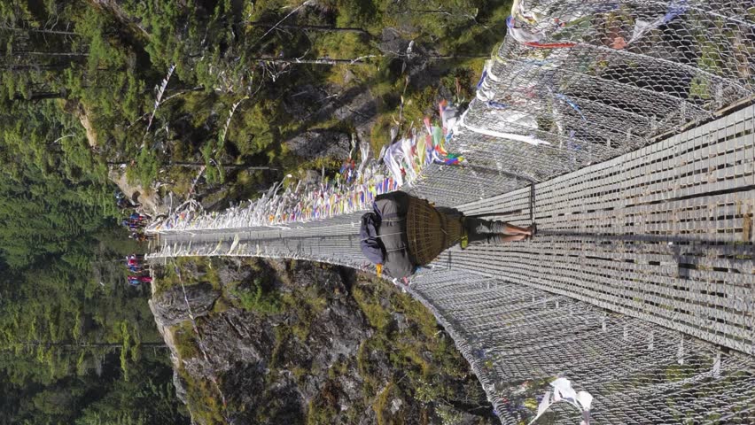 Porter is Walking on Suspension Bridge in Khumbu. Himalaya, Nepal. Slow Motion. Vertical Video