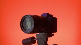 Professional photo camera stands on a tripod in a studio with color neon lighting. The photographer makes settings before shooting begins.