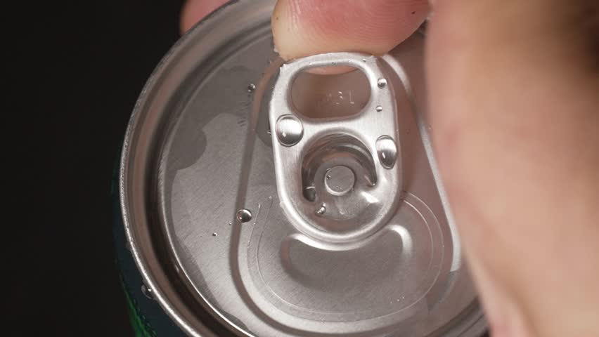 Hands close-up opening aluminum can with soda inside. Water drop droplets on metal jar. Food Beverage. Male hand opening shaking metal can of beer on black gradient background in slow motion.