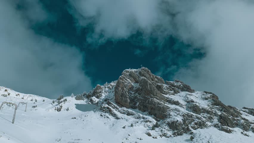 Over the peak of Engelberg, partly covered in snow, cloud formation is shot in a timelapse. Snow covers the slopes below the mountain Royalty-Free Stock Footage #3400049573