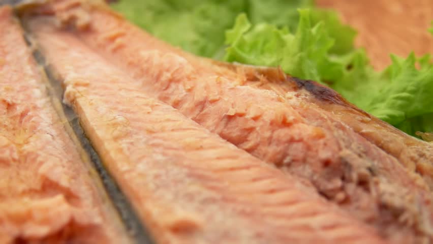 Super close-up panorama of the delicious juicy grilled red char fish on the greenery on the wooden plate. High quality FullHD footage