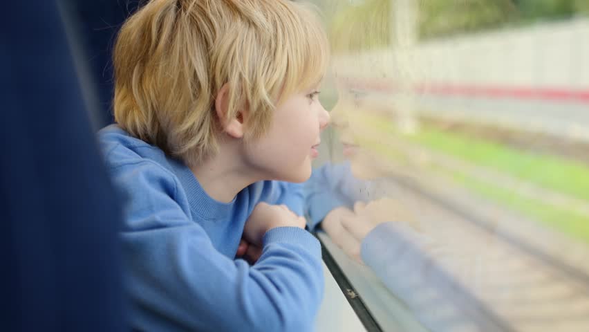 Cute teenage boy having fun during a ride in a subway train carriage or by rail. Child is watching the rain from the window. Close up portrait of the young passenger. Royalty-Free Stock Footage #3400203577