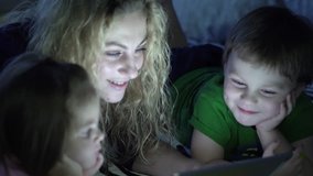 Family mother with young children playing games and watching cartoons on a tablet computer.

