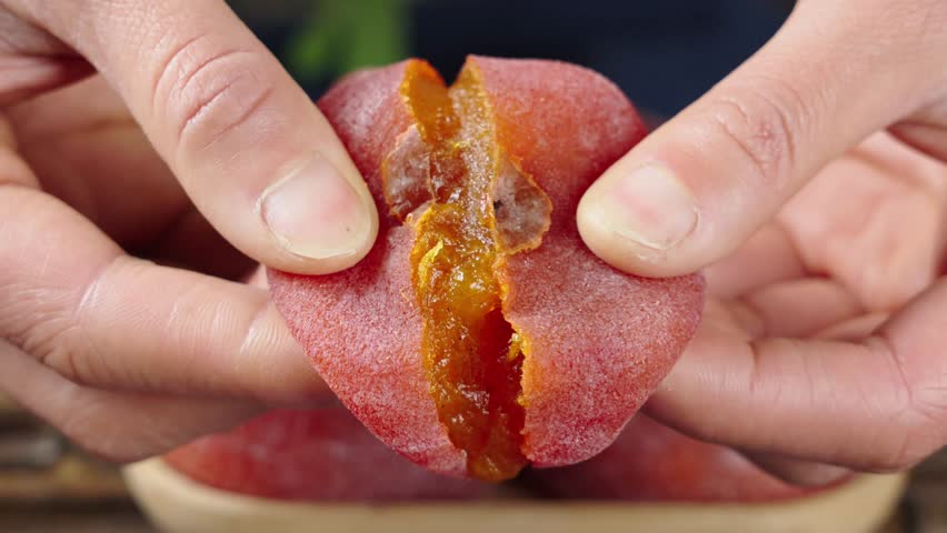 close up of hand split a dried persimmon on wooden table.