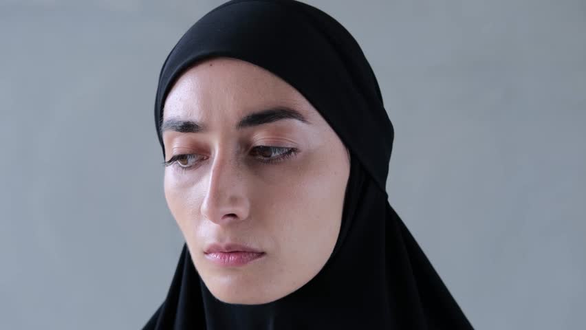 Muslim woman in black hijab looks sadly at camera. Close-up: sad face of Muslim woman in black hijab, huge brown eyes looking into camera. Concept: sad face of Muslim woman in black hijab Royalty-Free Stock Footage #3400400317