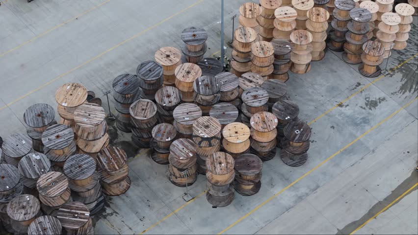 Drone footage showcases wooden cable drums neatly organized in an outdoor storage area. Overcast weather.