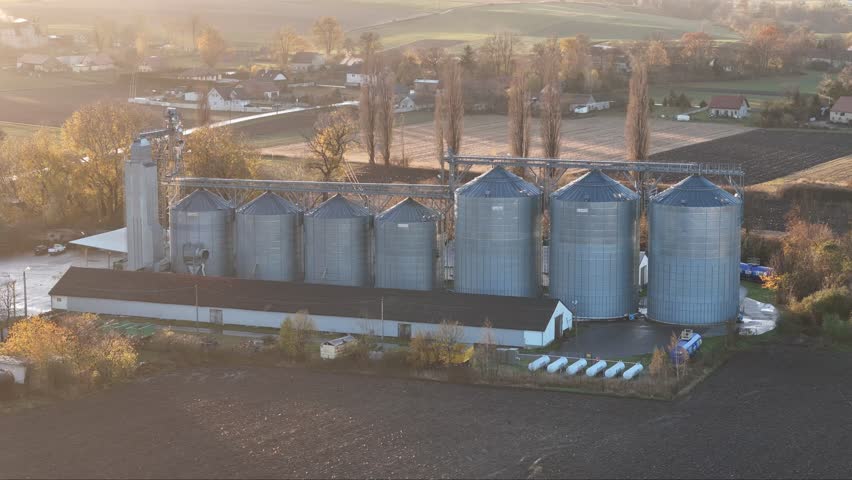 High above, modern silos stand amidst fields ready for winter, the setting sun casting a glow on them.