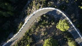 Drone following woman cyclist on road bike climbing uphill in mountains in Spain with long shadows. Female cyclist training on road bike. Sport cycling motivation drone video.Pedaling through the peak