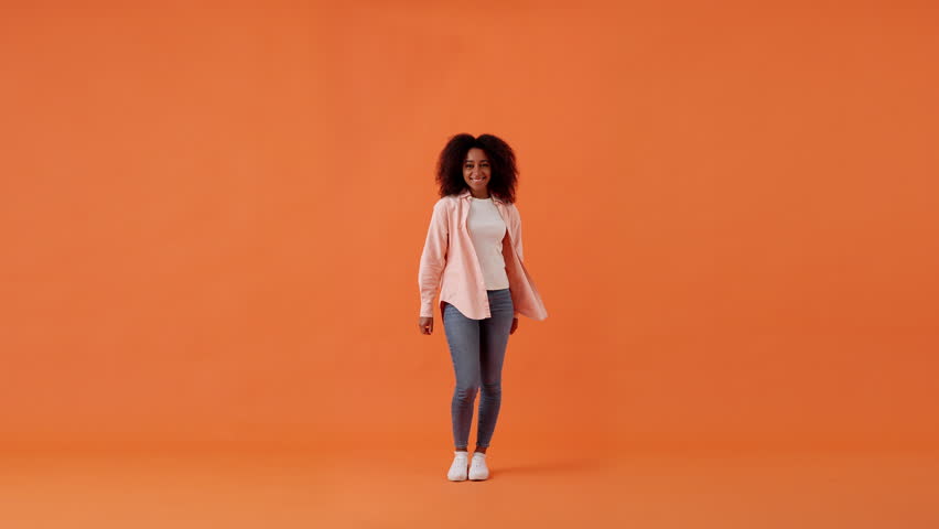 Cheerful African American woman jumps up enjoying moment of life in studio with orange background. Positive emotions and shooting in modern photo studio slow motion Royalty-Free Stock Footage #3400493283