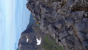 Aerial view of Man and woman at the top of the mountain. Beautiful view of the peaked tops of the Lofoten Islands. Norway, vertical footage