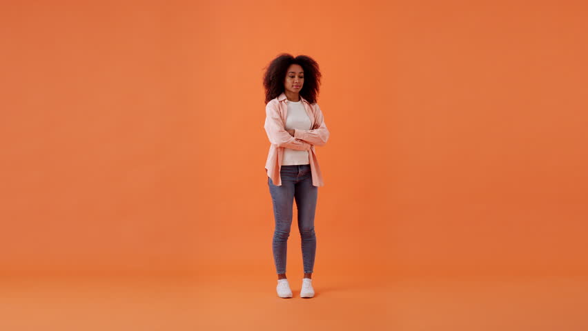 Pensive African American woman comes up with idea showing Eureka finger sign. Young lady brainstorming and genial thoughts in orange room. Full size