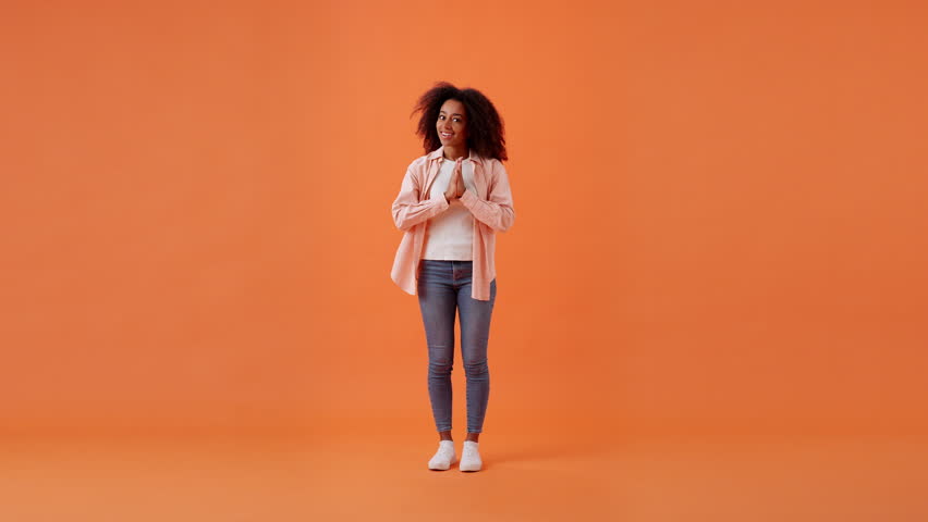 Pensive African American woman comes up with idea showing Eureka finger sign. Young lady brainstorming and genial thoughts in orange room. Full size