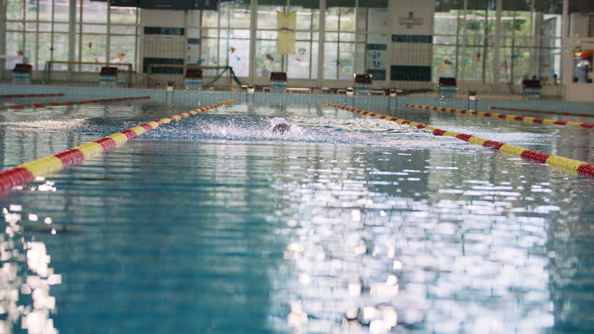 Successful professional female swimmer swimming butterfly stroke in the indoor lap pool, front view slow motion. Concept of determination and hard sports training.