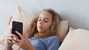 A charming young teenage girl is having an online conversation through her smartphone while in her room at home