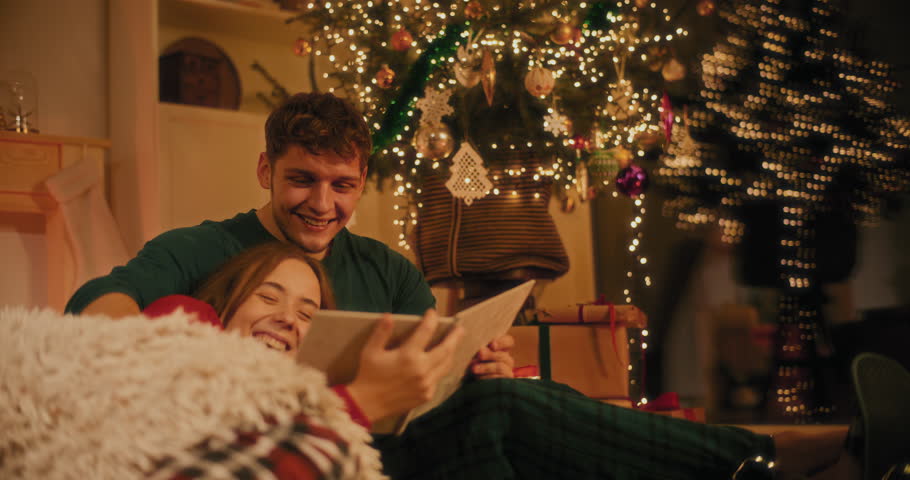 Happy young couple watching photo album at home during Christmas eve