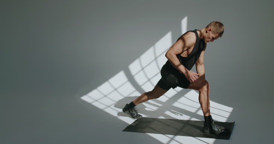 Young athletic man preparing body to workout and doing warm up exercises. Muscular male doing stretching on yoga mat in studio with white background