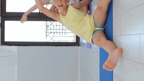 Vertical video. Mother with cute kids stretching on fitness mats, slow motion. Young woman with cute baby and older daughter working out indoors