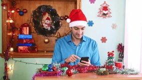 Handsome man in Santa hat sitting at home, chatting on his mobile phone at wonderful Christmas Day