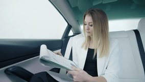 Businesswoman in an electric car examining annual reports, attentively viewing charts and flipping through them, Dressed in a white suit, sitting in a luxury car with white seats. 4k footage. - Powered by Shutterstock - Get 15% off with code: PIKWIZARD15