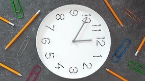 12 o'clock. Study or business time. Clock  with white clock face on dark background with big paper clips and pencils. Vertical Hyperlapse.