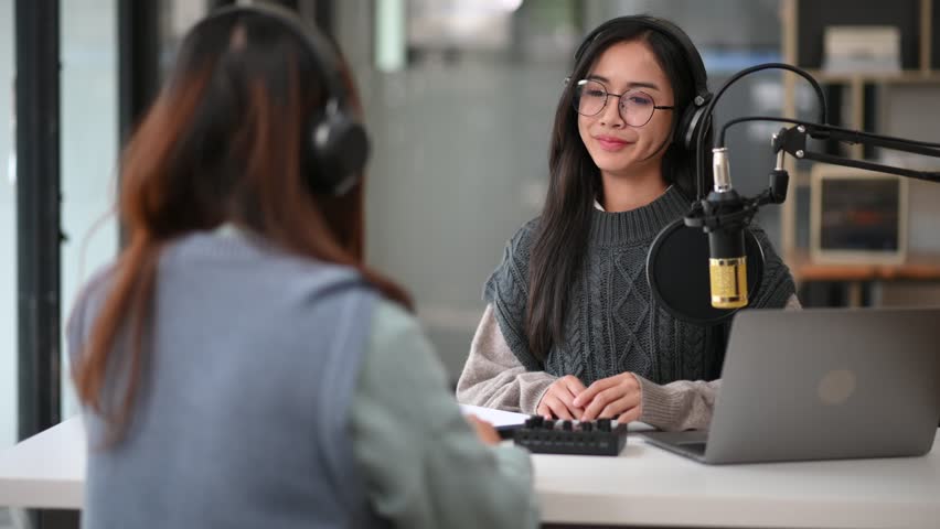 Young woman and woman wearing headphones and doing a live podcast for their channel, communication for radio podcast and technology concept
