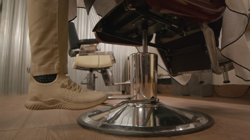 Cropped shot of legs of unrecognizable hairdresser pushing pedal of chair to lift it up before serving client in barbershop
