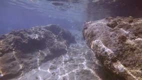 Camera moving forwards along rock above seabed with large stones covered with algae in coastal area on bright sunny day, Slow motion. Underwater seascape of Mediterranean Sea, Greece