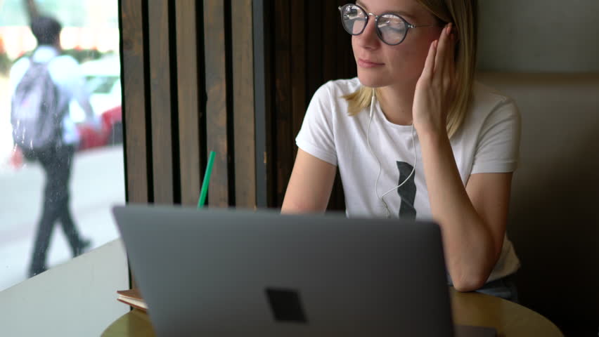 Young creative female copywriter typing text for web page content enjoying music playlist in earphones, caucasian woman working distantly on netbook in cafe interior | Shutterstock HD Video #34015729