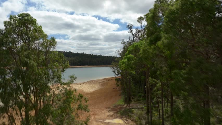 Rising drone out of the forest to show a large lake in Western Australia, tilting down as drone ascends.