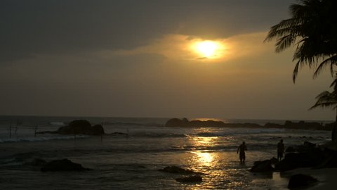 Silhouette of two people who walk along the seashore at sunset.