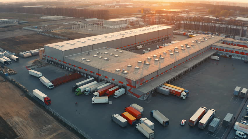 Aerial all-round view of a logistics park with a warehouse. Loading hub with many semi trucks with cargo trailers standing at ramps for loading and unloading goods at sunset Royalty-Free Stock Footage #3401649927