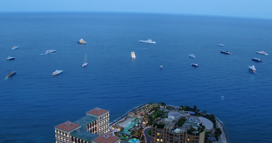 Aerial Shot Of Passenger Crafts Floating On Wavy Sea, Drone Flying Backwards Over Modern Buildings At Night - Monte Carlo, Monaco