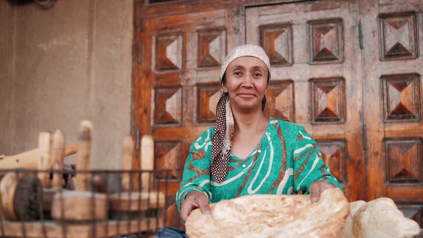 Eastern woman prepares flatbread using traditional method. East market. Elderly asian woman in colorful national clothes prepares bread. Uzbekistan, Khiva. Royalty-Free Stock Footage #3401740111